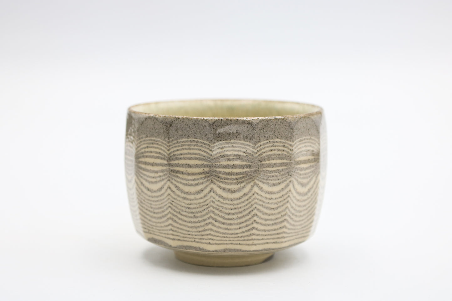A ceramic tea bowl with a textured, wavy pattern in earthy beige and gray tones, set against a plain white background.