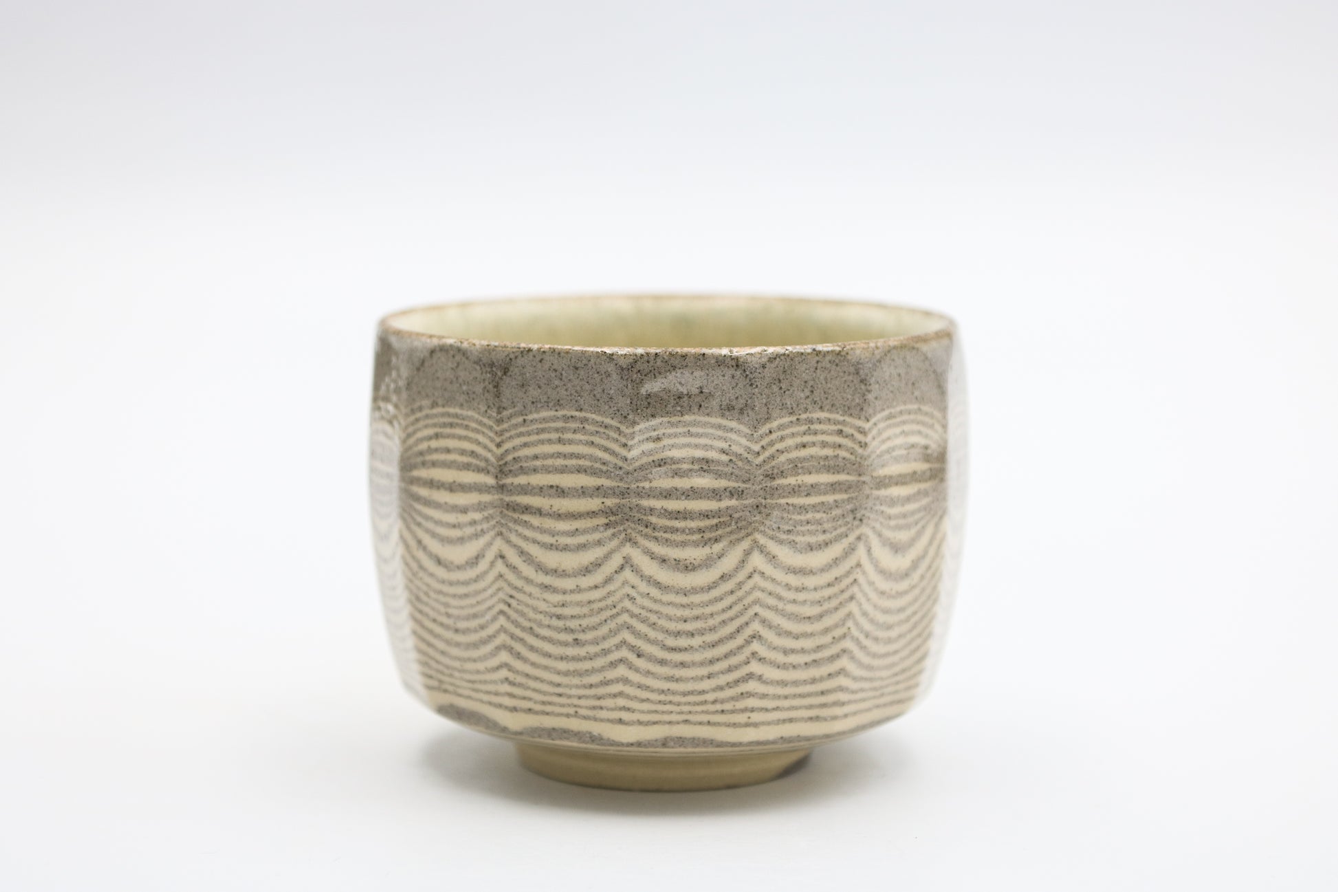 A ceramic tea bowl with a textured, wavy pattern in earthy beige and gray tones, set against a plain white background.