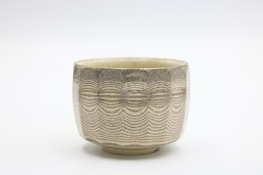A ceramic tea bowl with a textured, wavy pattern in earthy beige and gray tones, set against a plain white background.